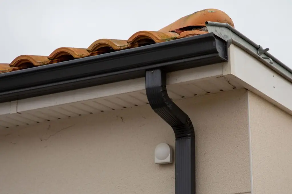 metal black gutter on home roof covered with ceramic tiles Close