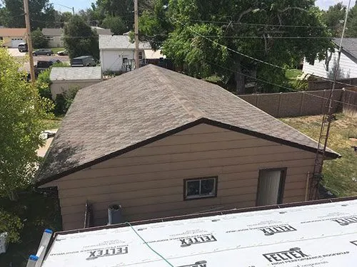 Aerial view of a completed shingle roof on a detached garage with underlayment visible on adjacent structure
