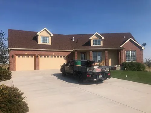 Brick home with dark shingle roof and dormer windows, work truck parked in the driveway