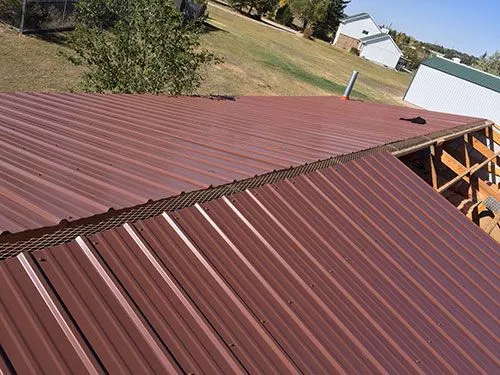 Red standing seam metal roof panels installed with ridge vent, overlooking farm buildings