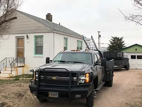 Work truck with ladder rack parked outside a white brick home with a shingle roof