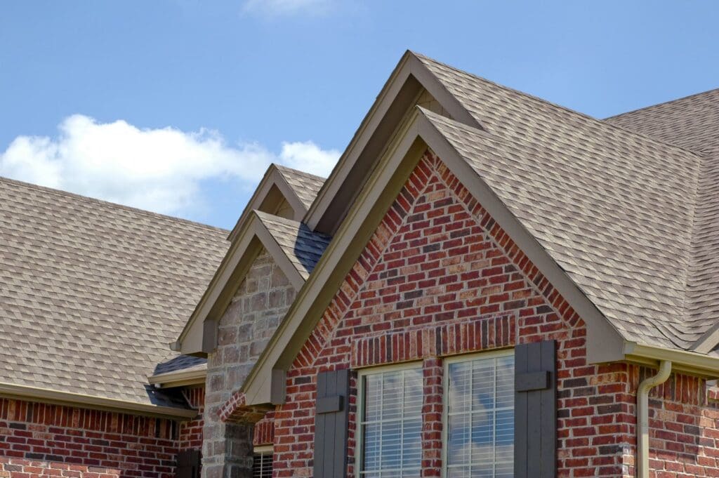 Seamless beige gutters along a brick home's roofline, with layered gable peaks and asphalt shingle roofing
